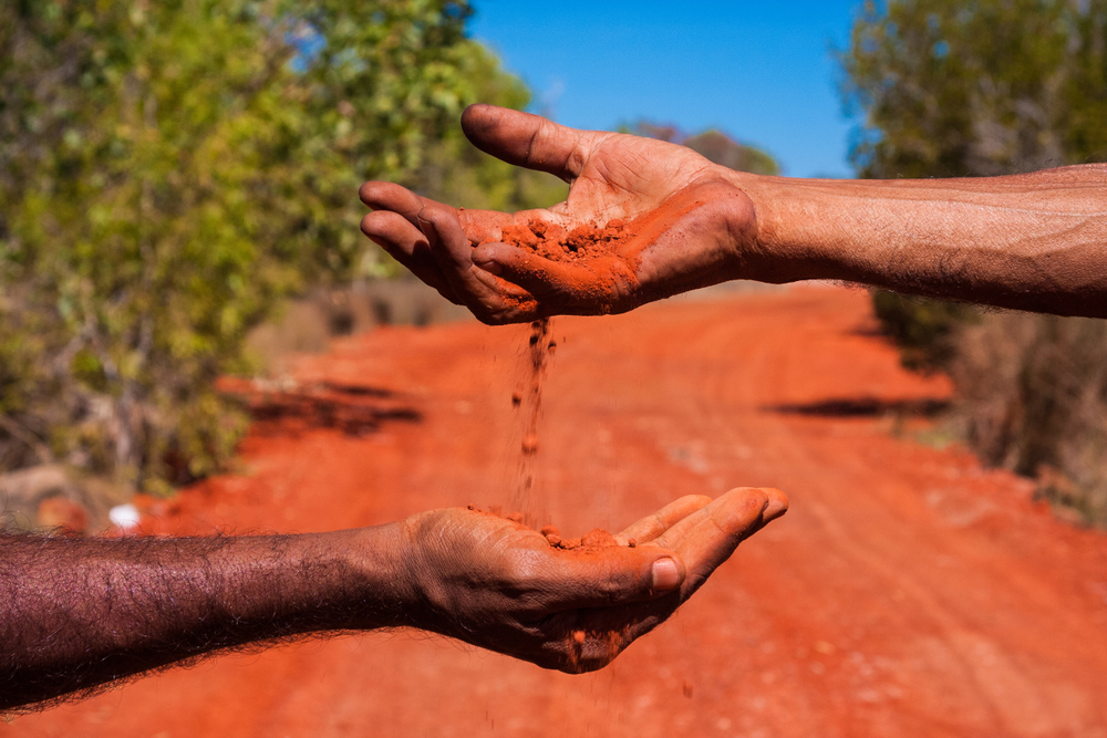 Australian outback background. Two hands passing red soil from one to another. Concept of Aboriginal people passing on values to next generation.