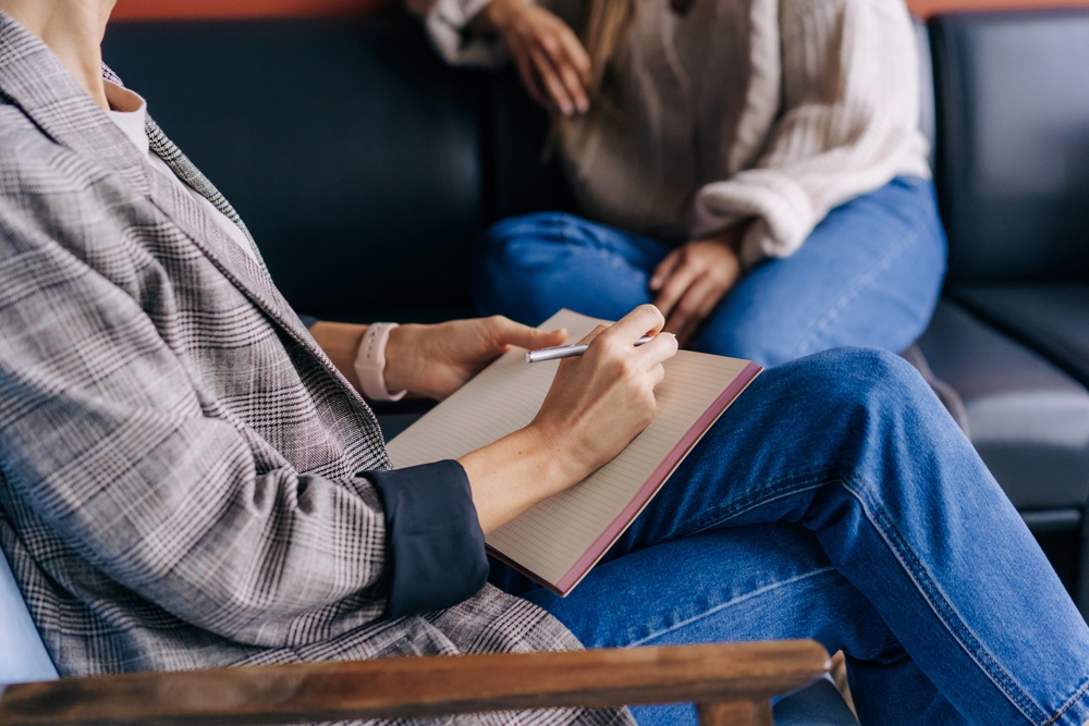 Close-up of a councilor's hands writing down notes in a notebook whilst talking to a client.