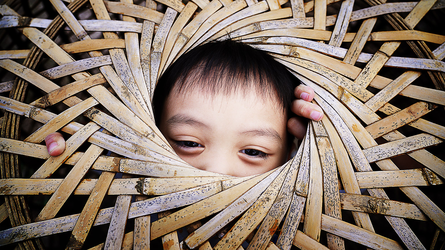 A young child peeking out of a traditional basket weaving