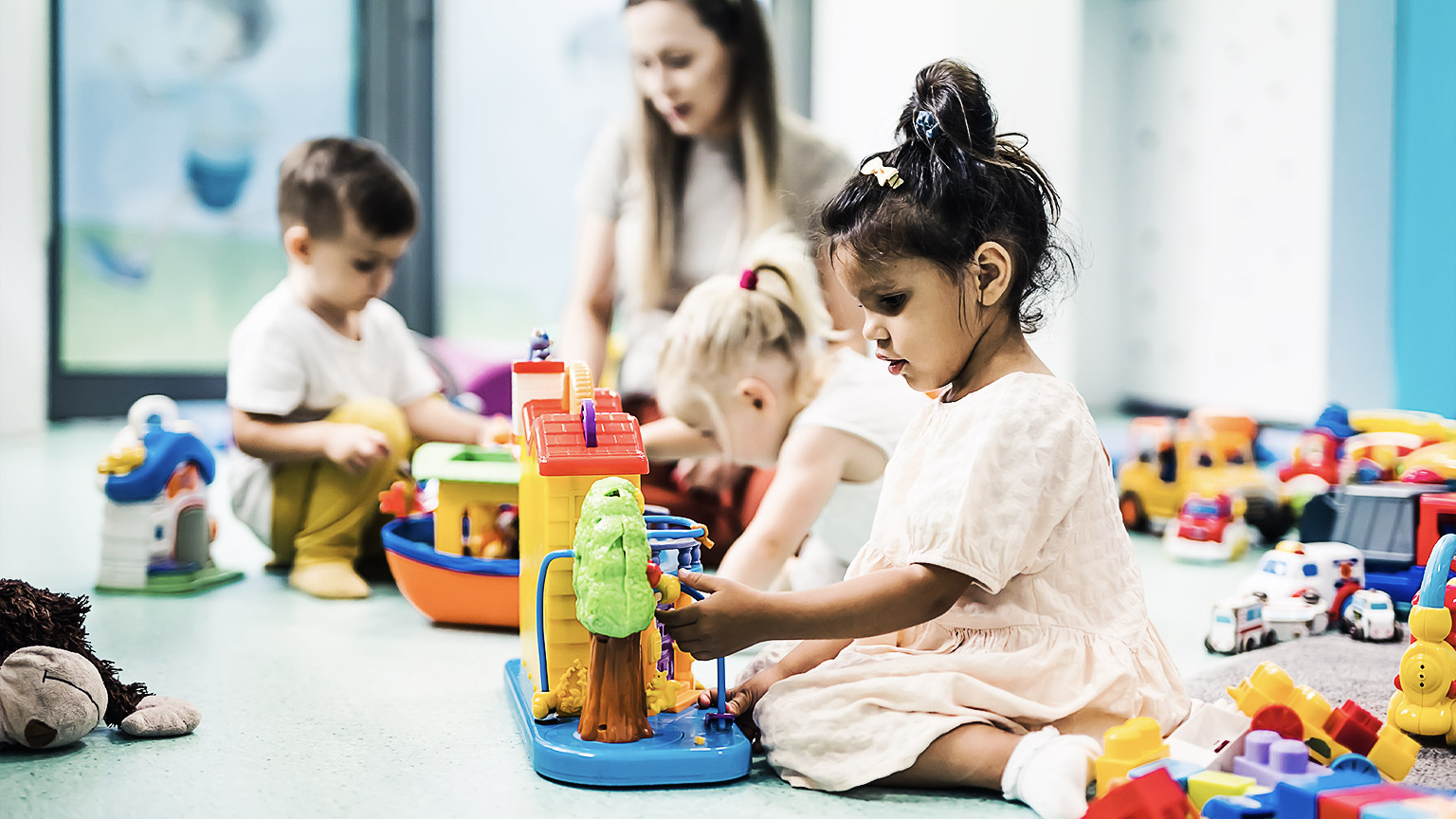 A homebased childcare setting with a baby playing on the floor and a young child from behind. 