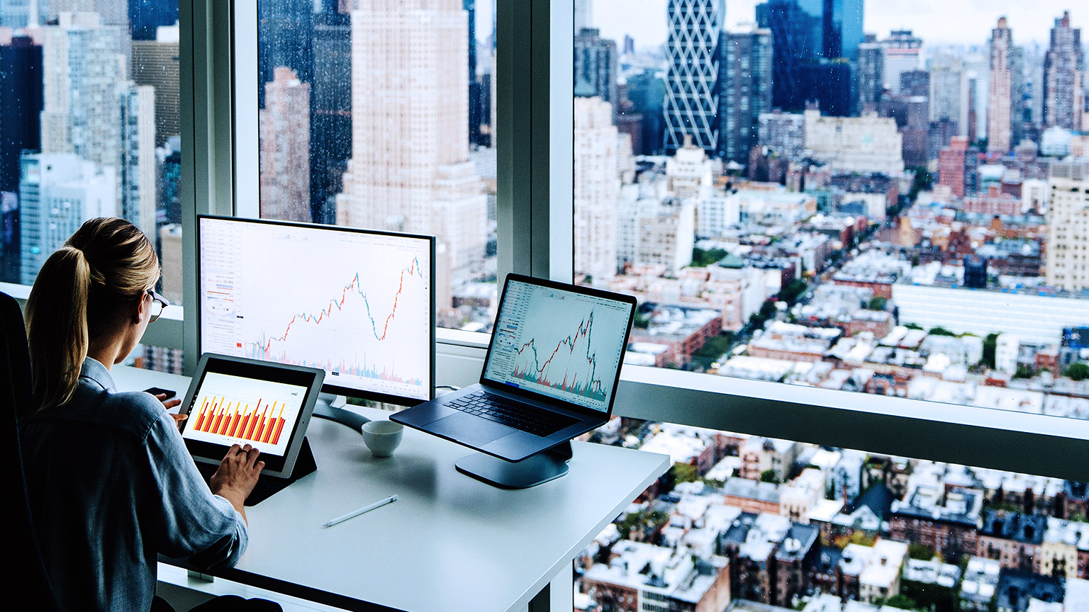 Back view of business woman sitting at panoramic skyscraper office desktop with financial graphs and statistics on monitor