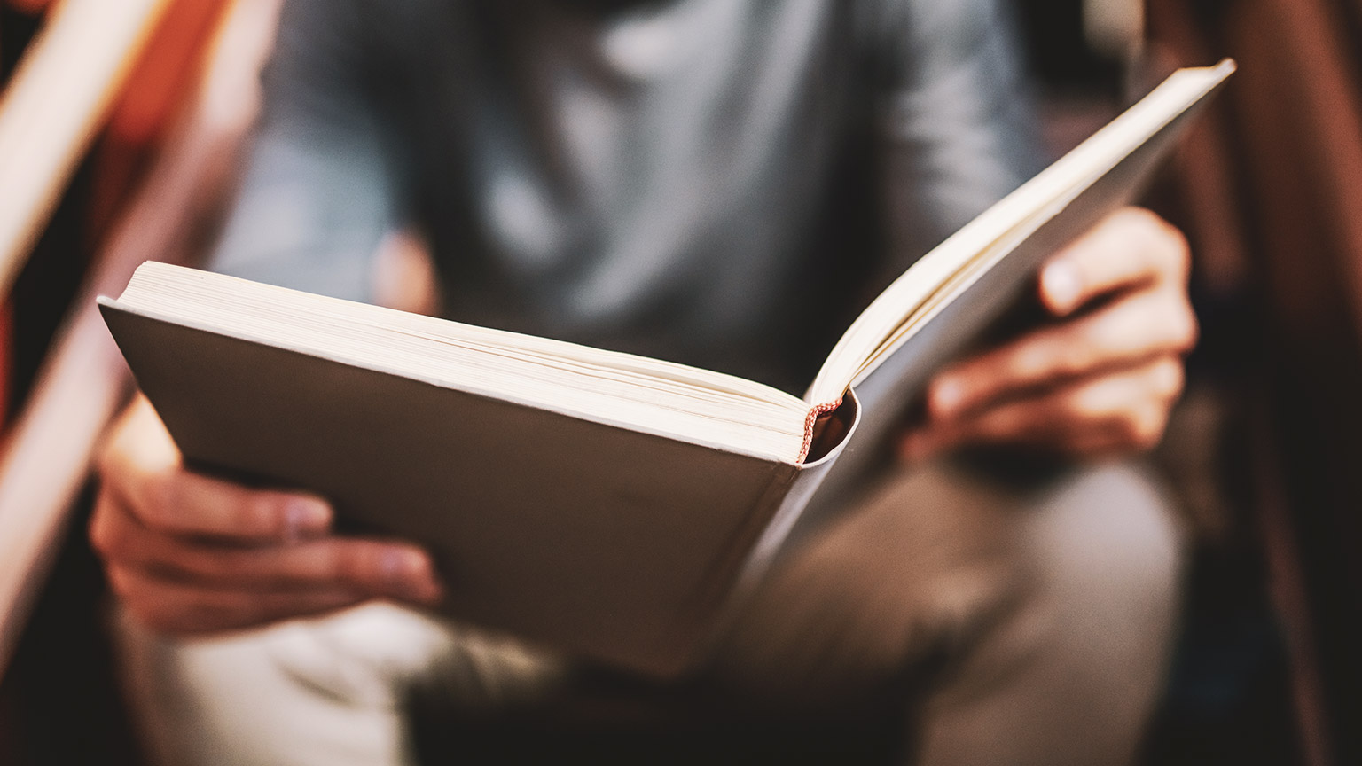 A close view of a person sitting in a library reading a book