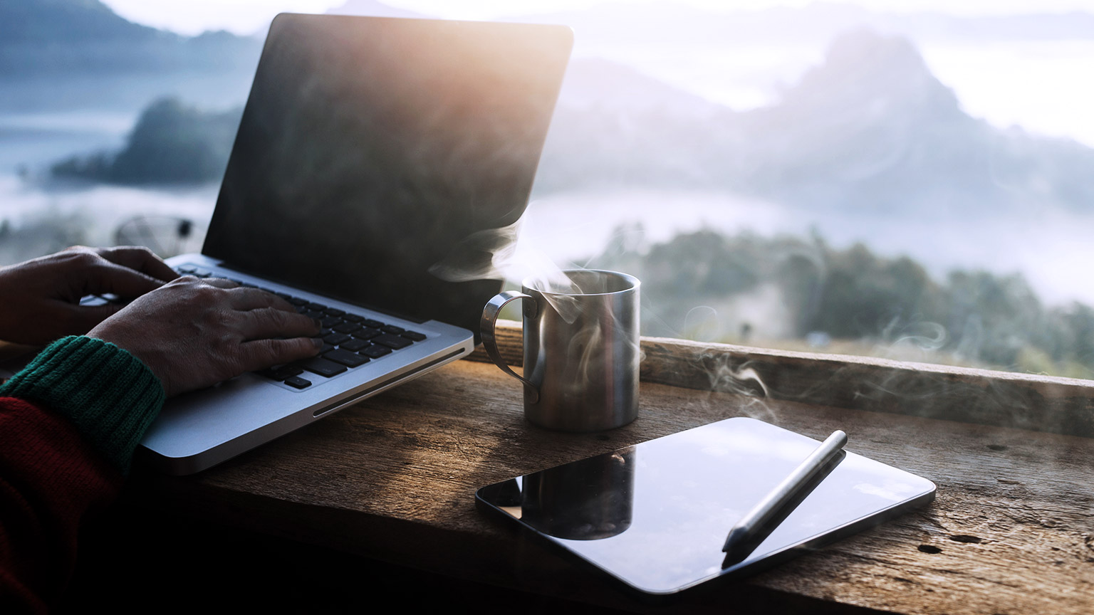 Man working on computer with coffee and mountain view