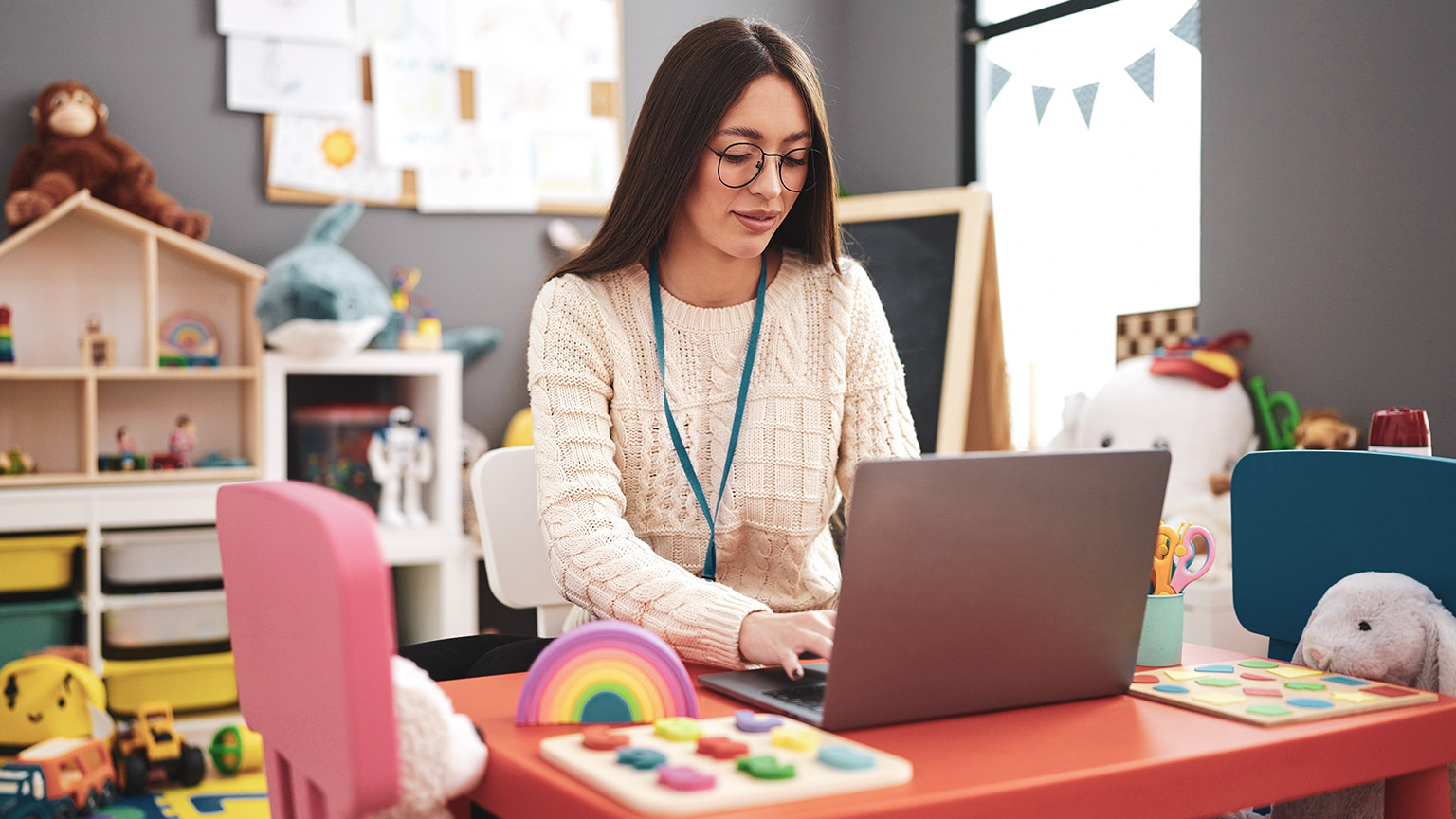 A teacher writing class notes on a laptop in a childcare centre