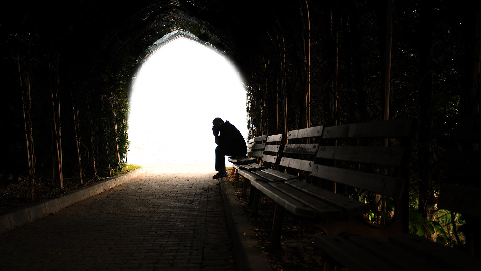 A wide shot of a person sitting on a bench at the end of an archway