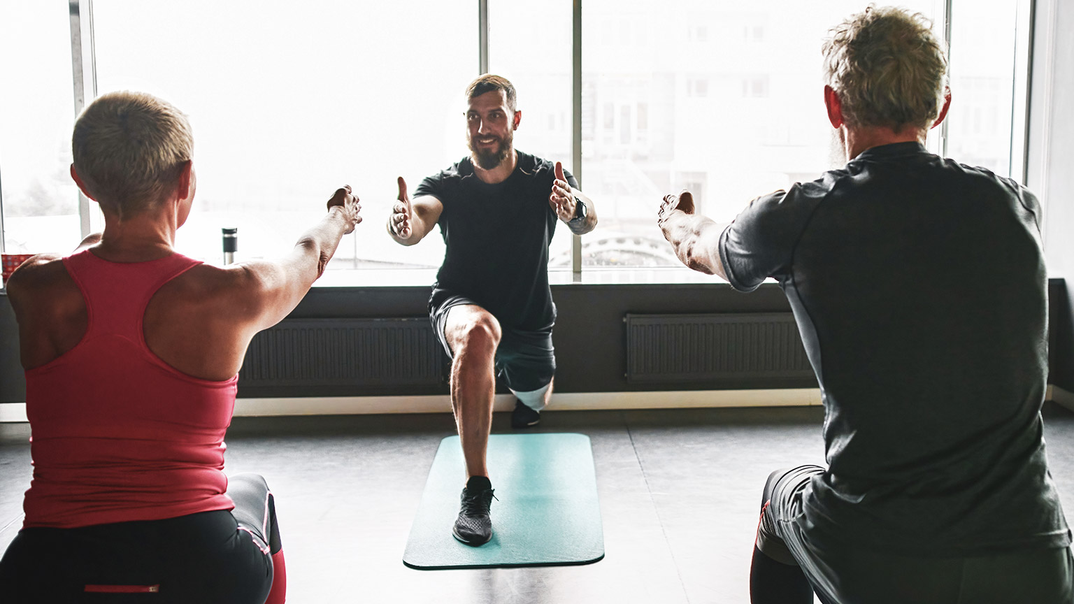 A trainer demonstrating an exercise for 2 mature clients