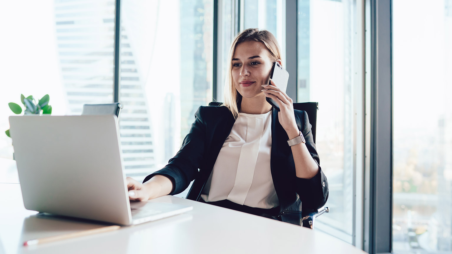 A business manager sitting in a modern office reading material on a laptop