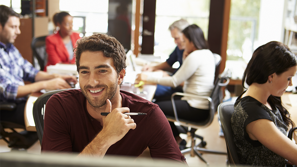 Businessman Working At Desk With Meeting In Background