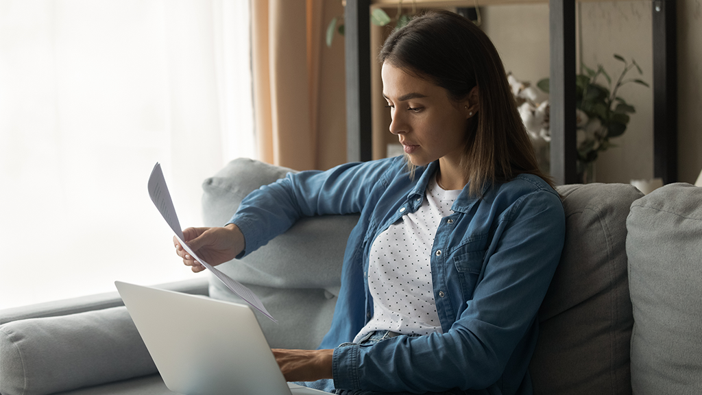 Serious millennial woman sit on couch hold laptop work