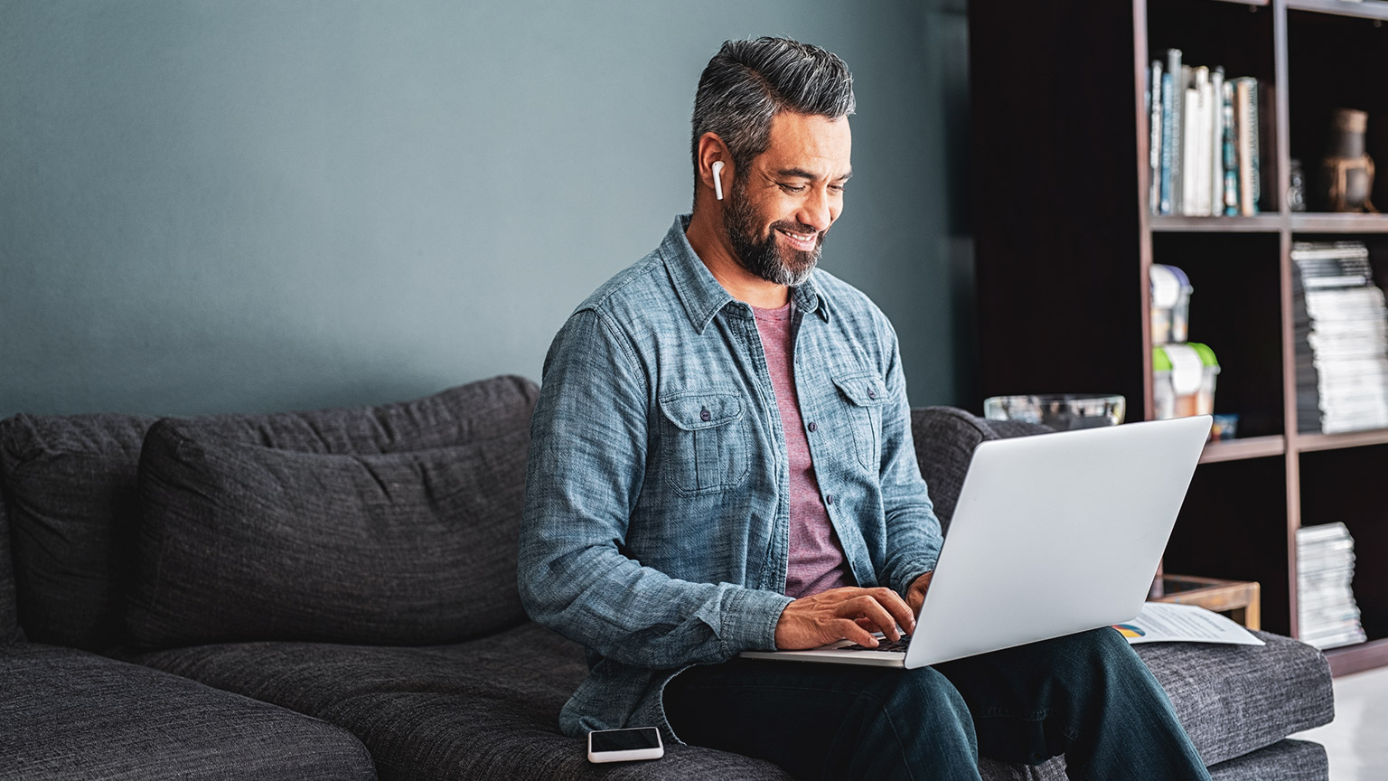 Man sitting on a lounge, smiling whilst using a laptop