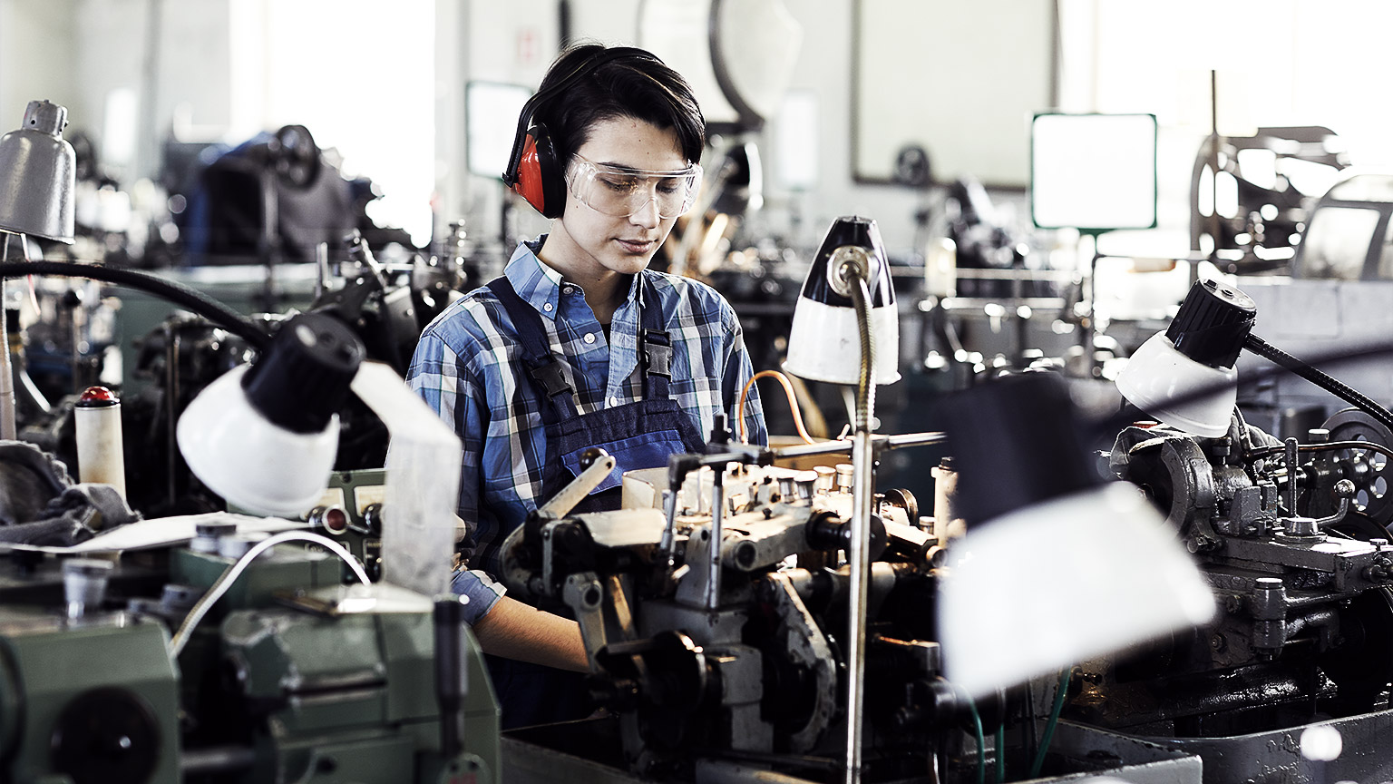 Serious concentrated young female engineer in ear protectors and safety goggles