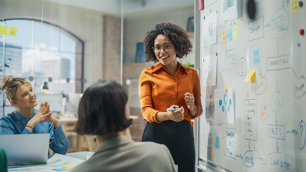 a woman presenting on a whiteboard with her colleagues