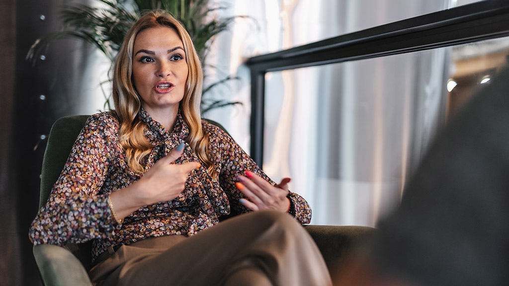 Serious adult woman sitting on the sofa while talking and explaining something with her hands to the man at the office