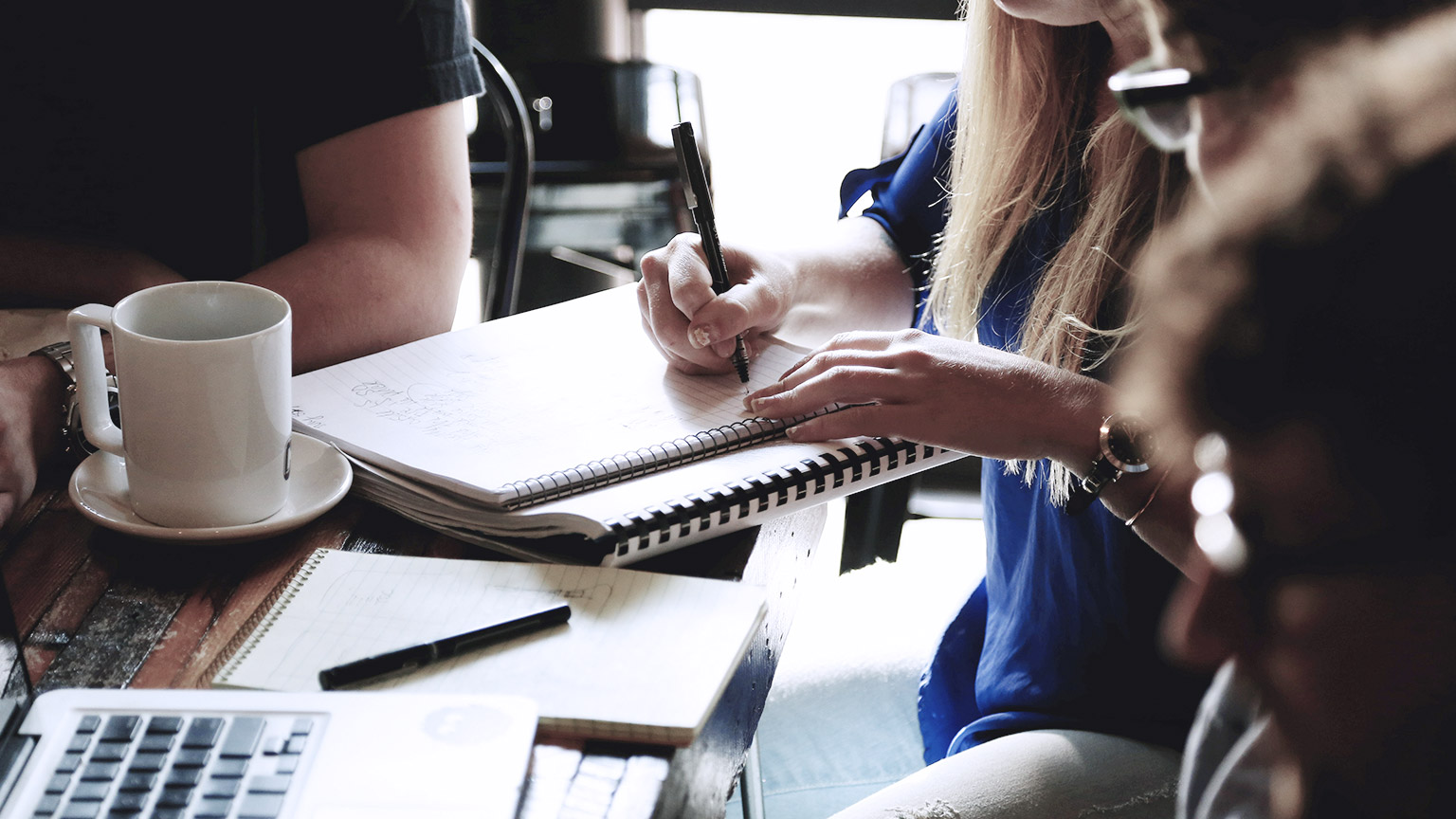 Woman taking notes on notebook with friends around her