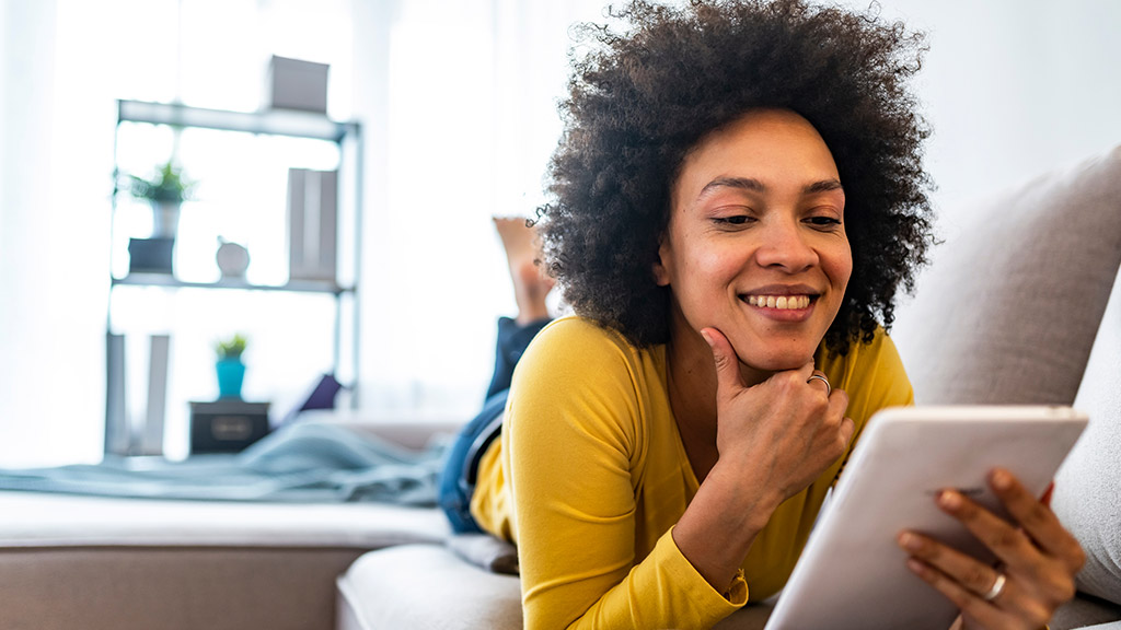 Happy young woman with tablet pc laying on sofa.