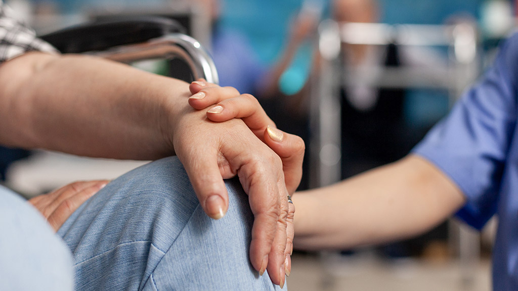 Social assistant worker consoling patient touching hands during homecare service