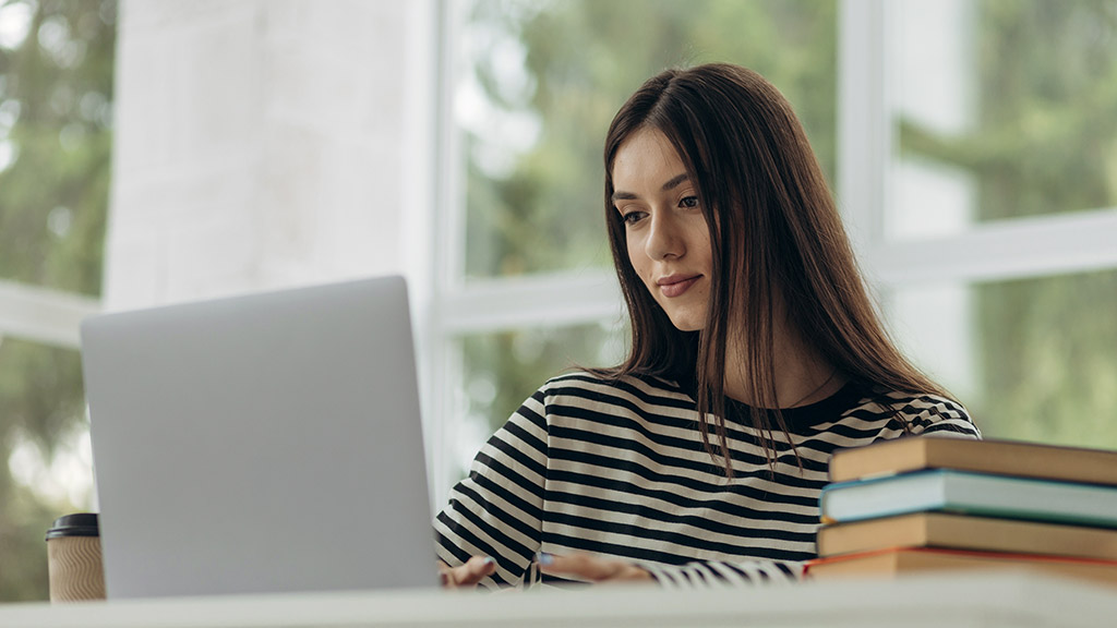 young woman studying sitting at table with laptop and books at home