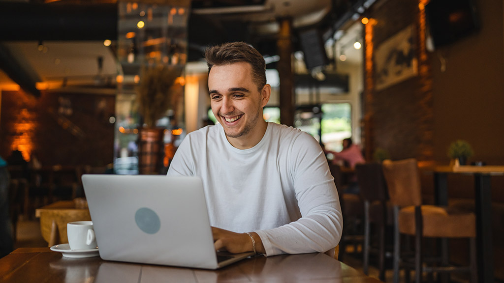 One man young adult caucasian freelancer male working online on his laptop computer while sitting at the table at cafe