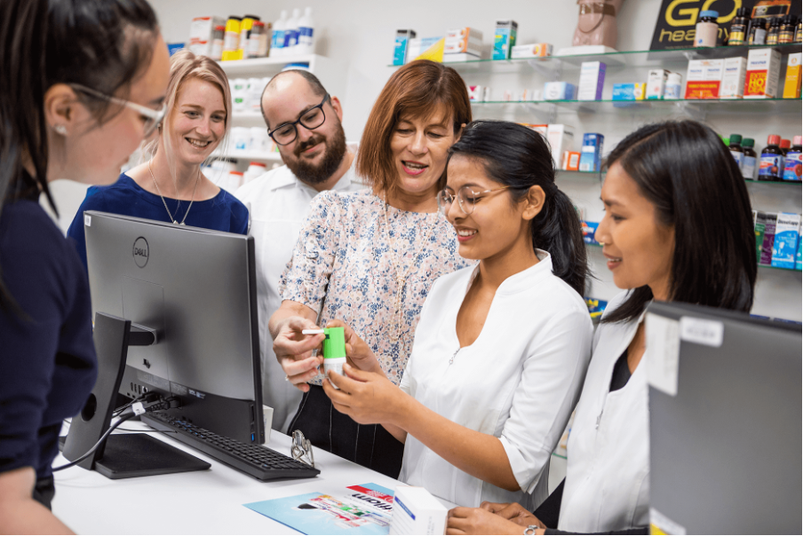 Six people stand around the pharmacy counter discussing an inhaler