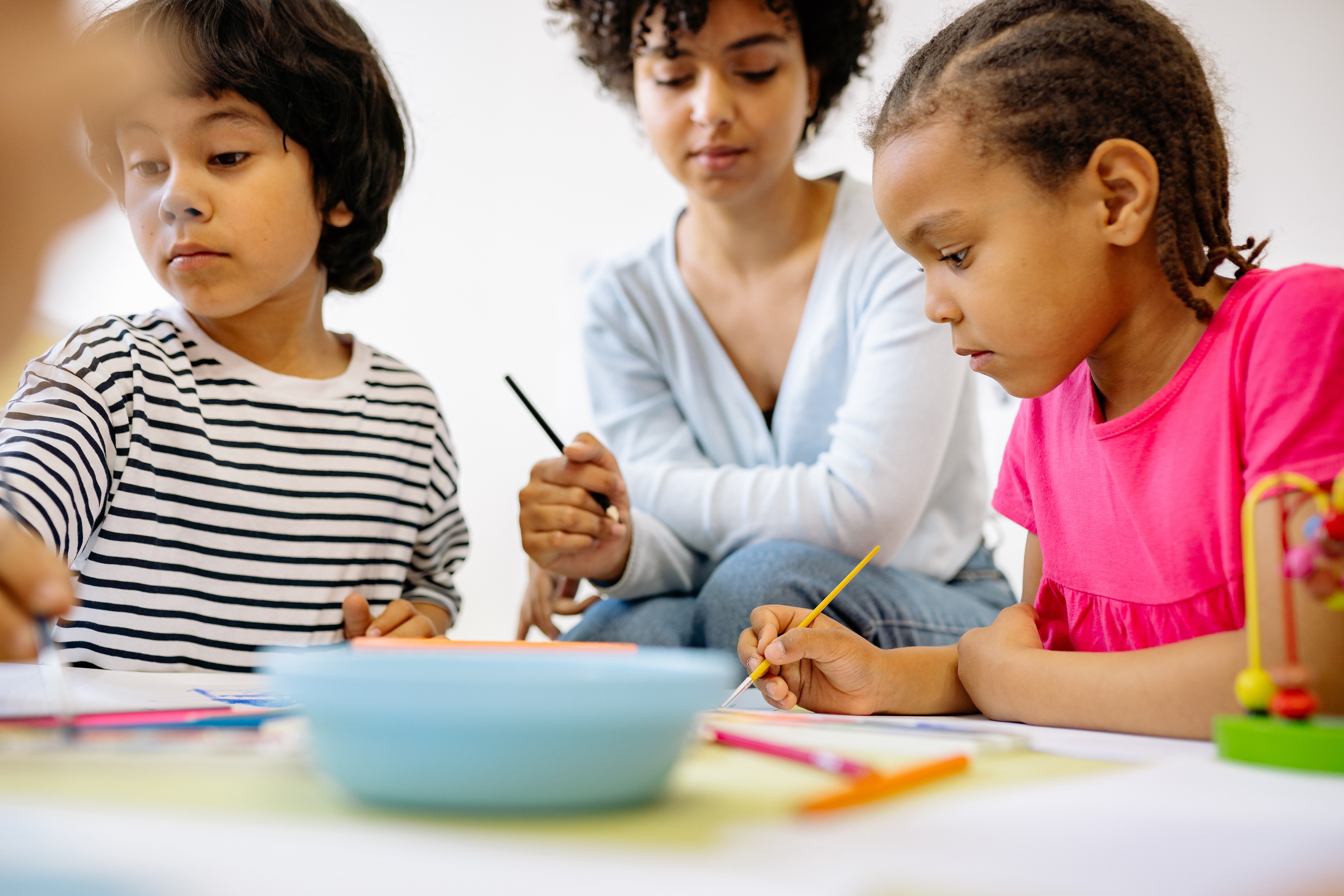 A young teacher with two under five children doing crafts at a table.