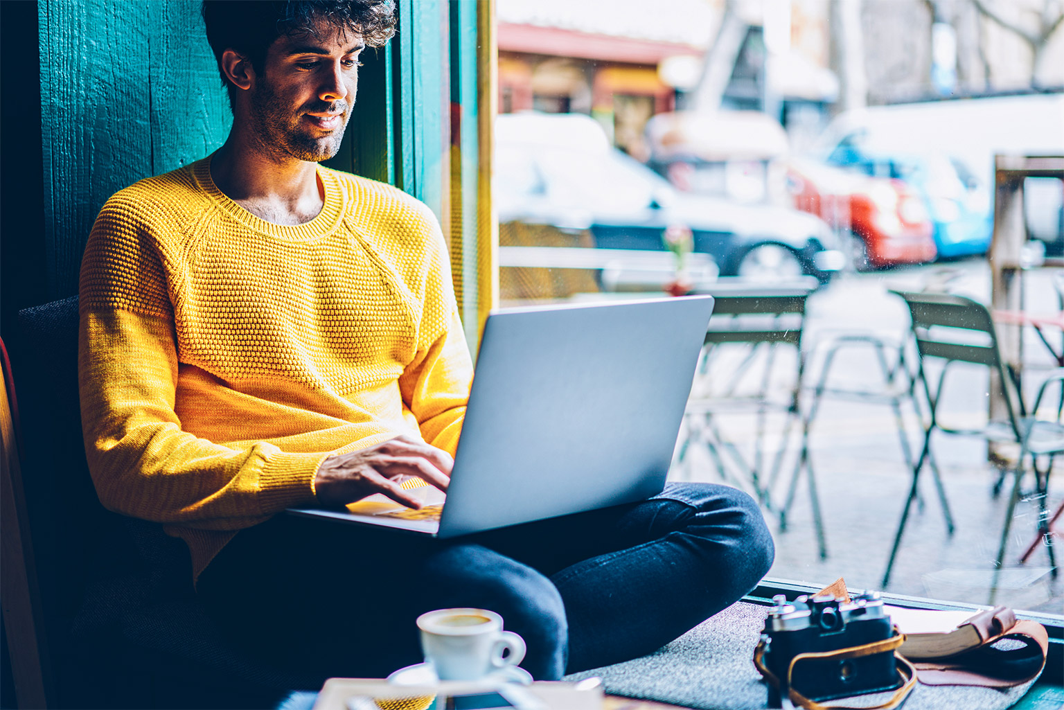 Person in a yellow jumper sitting in a window on a computer