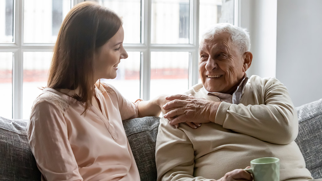 Smiling young woman sitting on sofa with happy older retired 70s father