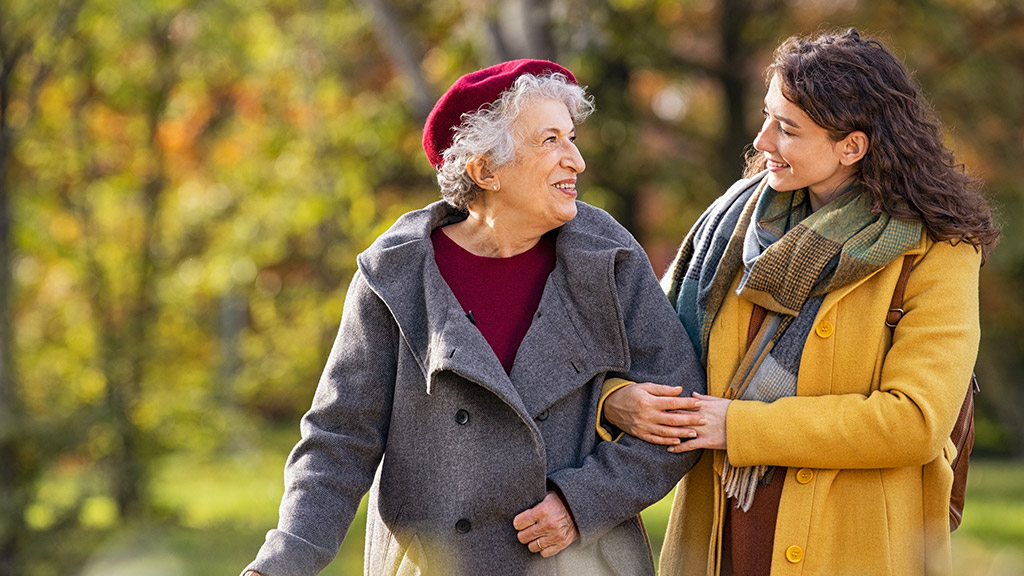 Young woman in park wearing winter clothing walking with old grandmother