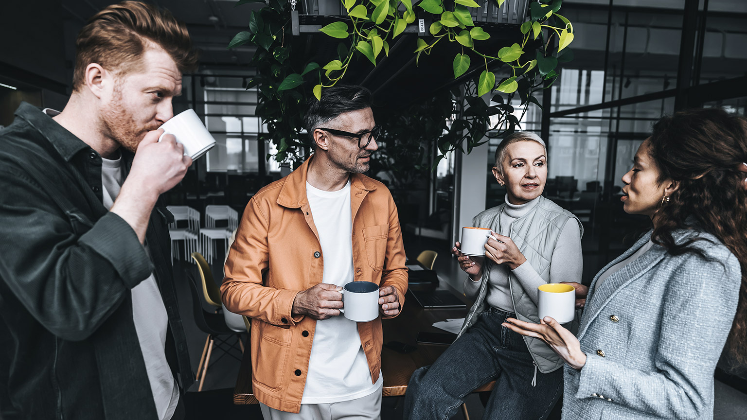 Multicultural workers talking while standing, sipping coffee