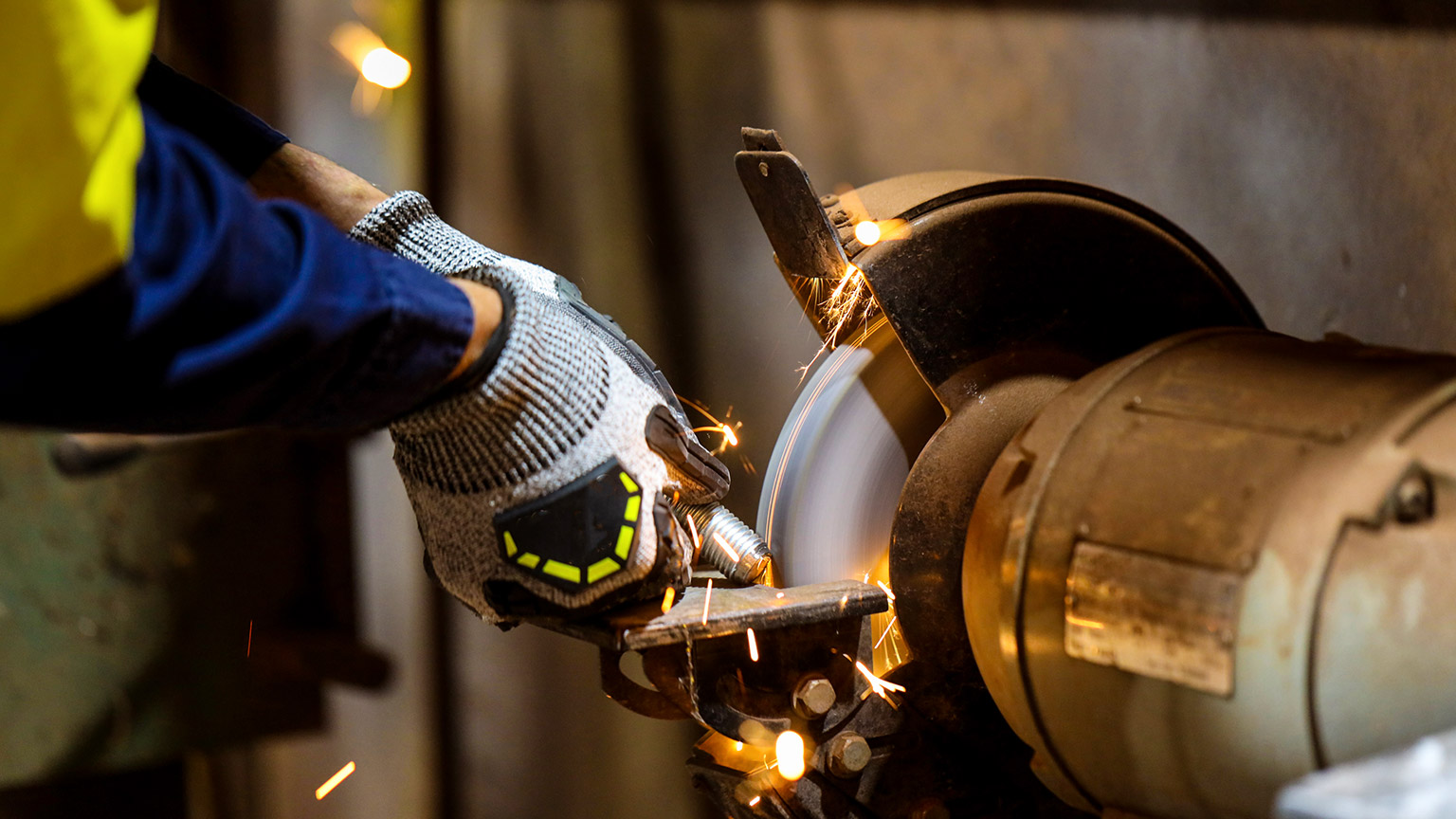 A close view of a person using a table grinder while wearing PPE