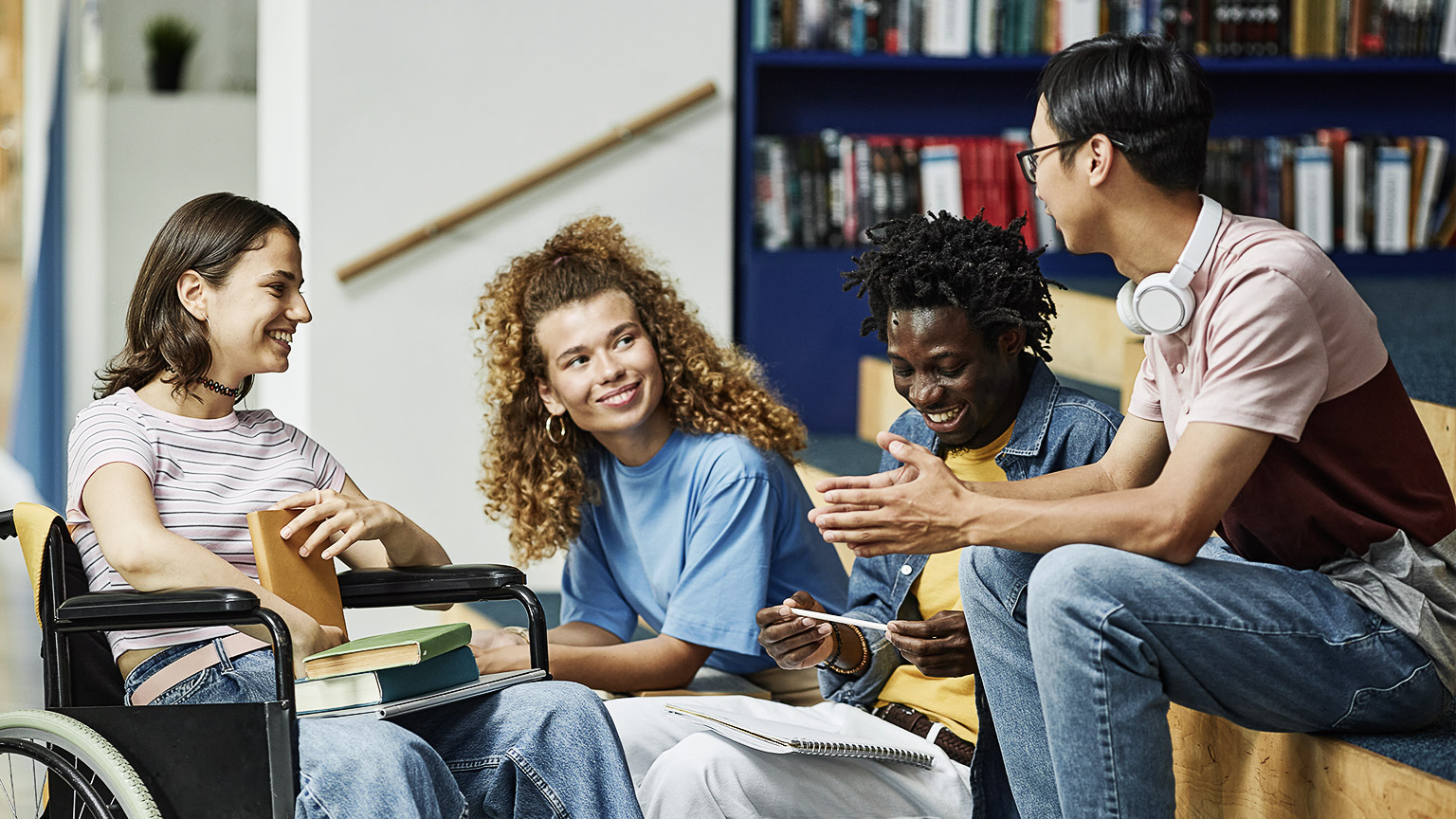 Diverse group of young people chatting in college library including female student with disability