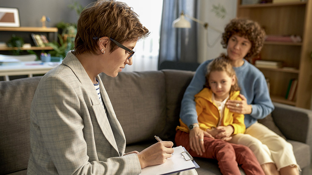 Social worker making notes in document while talking to child and his mom at home