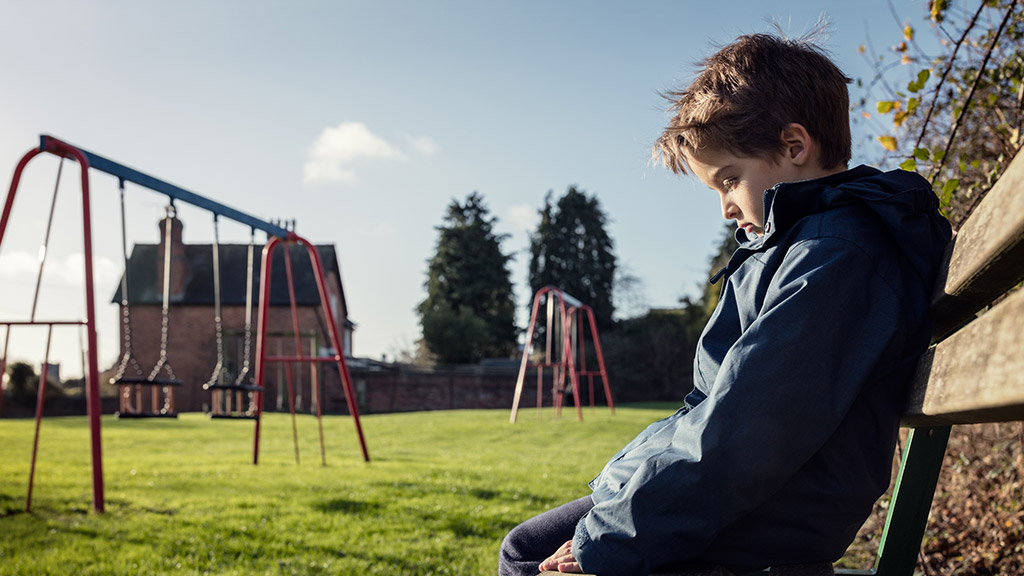 Upset problem child sitting on play park playground bench concept for bullying