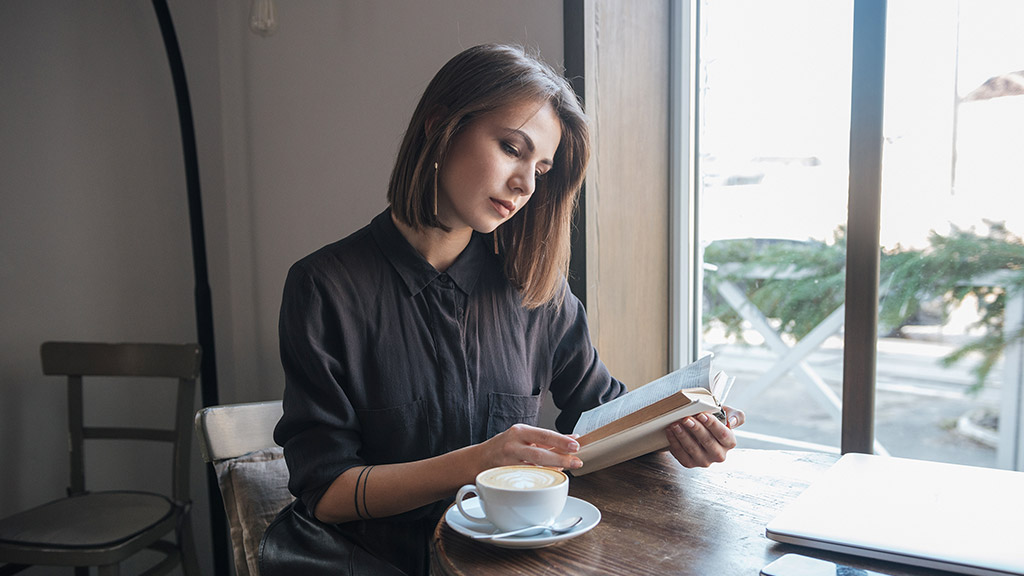 Picture of young pretty woman sitting at the table in cafe and reading book