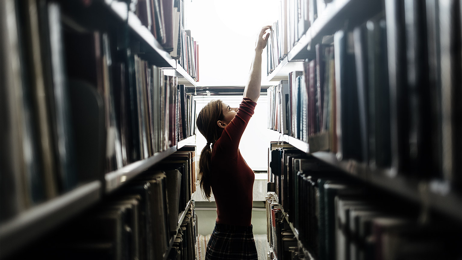 A person reaching up a bookshelf in a library