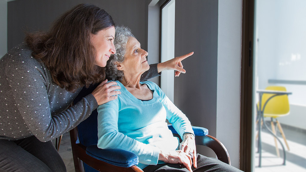 Adult daughter showing to senior mother scene out of window