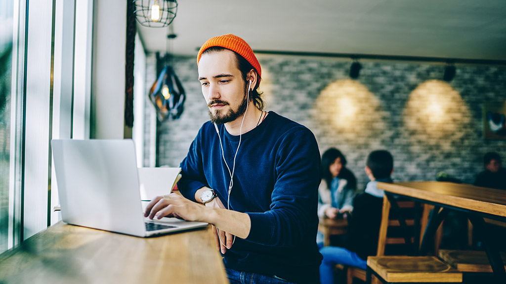  male resting in coffee shop listening favourite music in headphones and working with his laptop