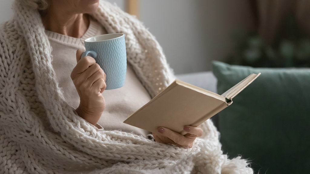 Elderly sitting on a chair with coffee while reading a book