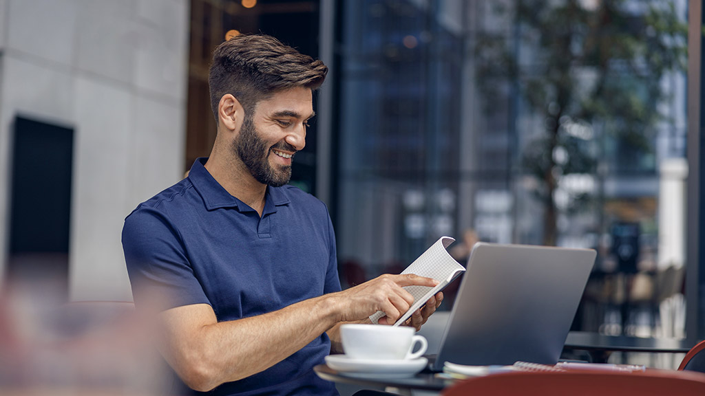 man looks at the notepad while working on laptop in cafe