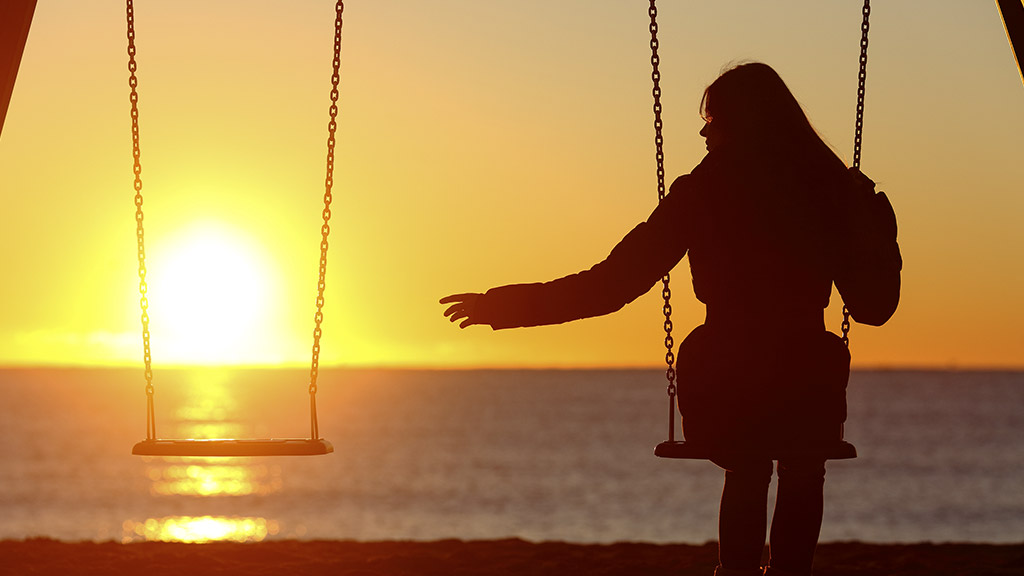 woman alone missing her love one while swinging on the beach at sunset