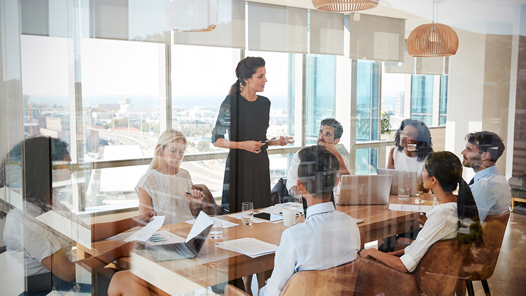 Businesswoman Leads Meeting Around Table Shot Through Door