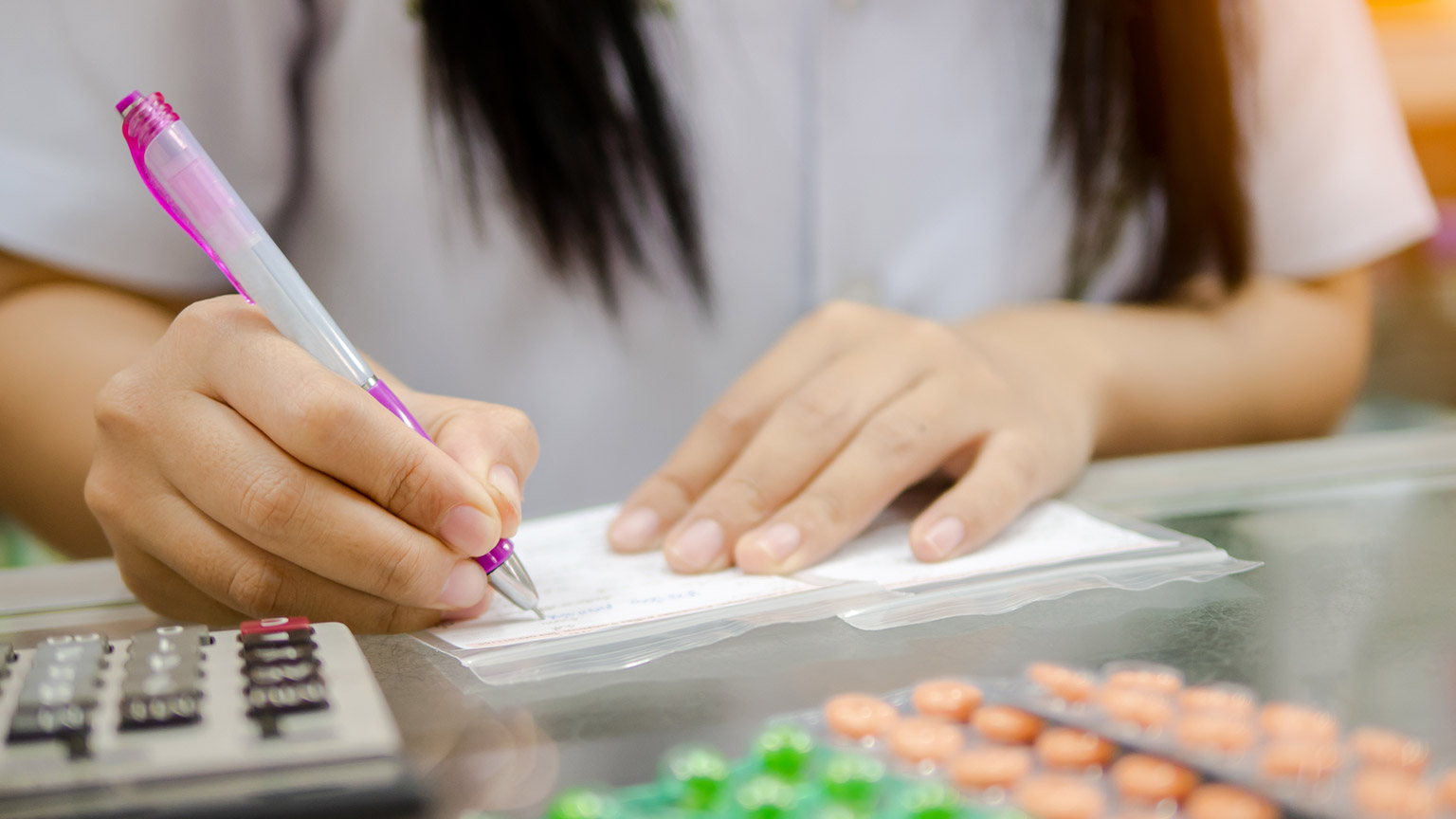 Pharmacist hand writing prescription to patient on blank label while explain and dispense many colorful pills and tablets in package close up.