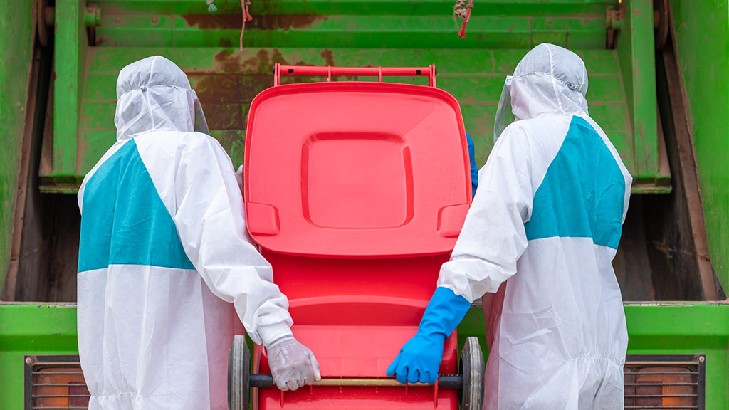 worker wear PPE protective clothing against corona virus of Infectious waste garbage collector truck loading waste and trash bin.