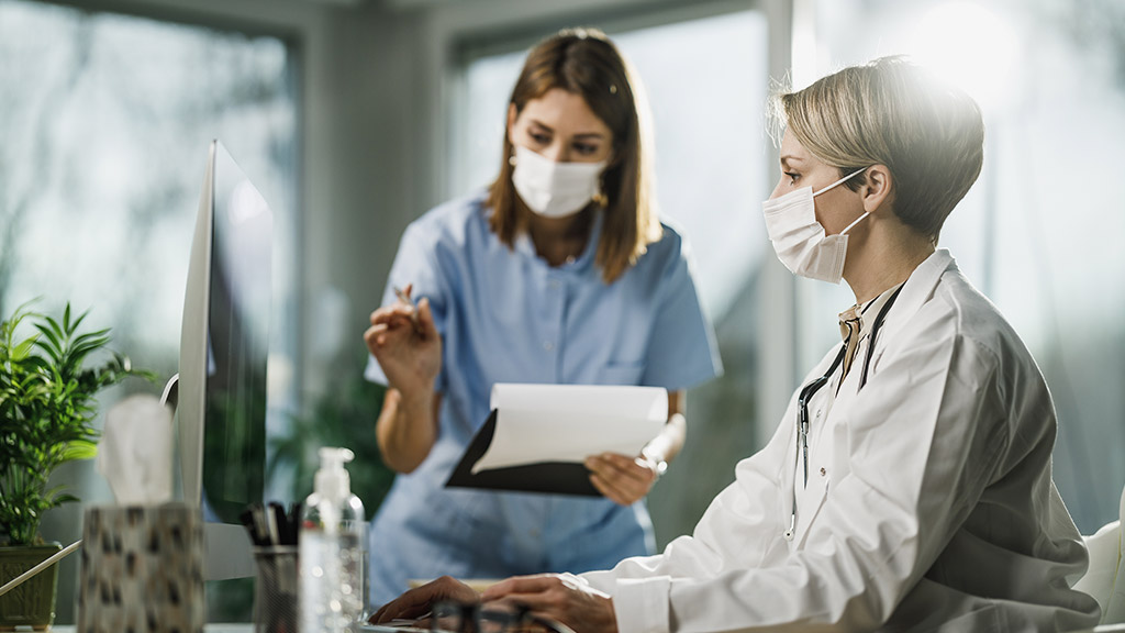 female doctor and young nurse working together on computer in consulting room