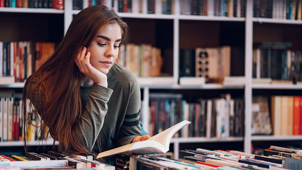 Young female customer reading a book in bookstore while buying some good literature