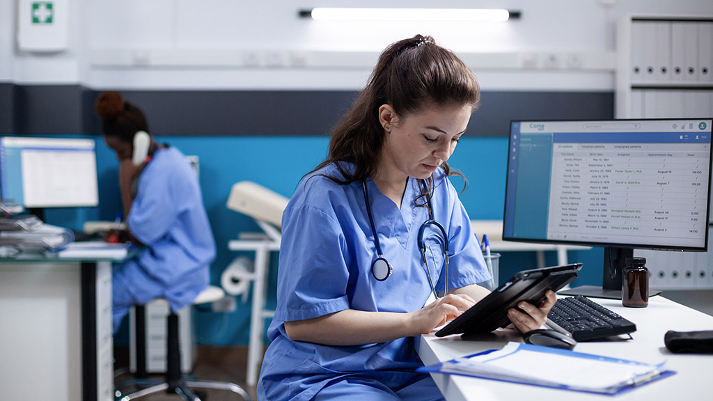 Young nurse checking appointments list on digital tablet in busy medical office