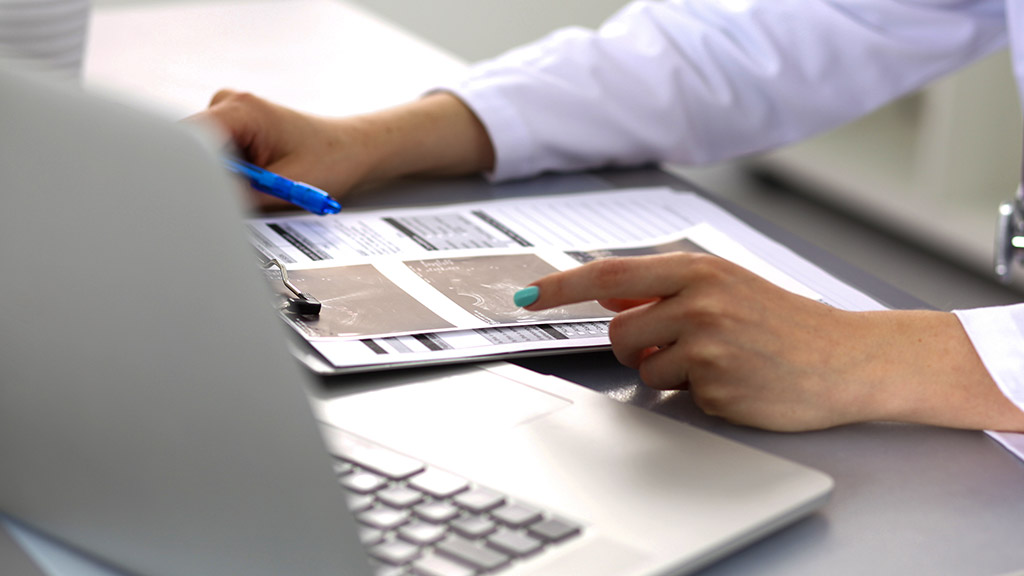 a young doctor assessing patient records using documents and laptop