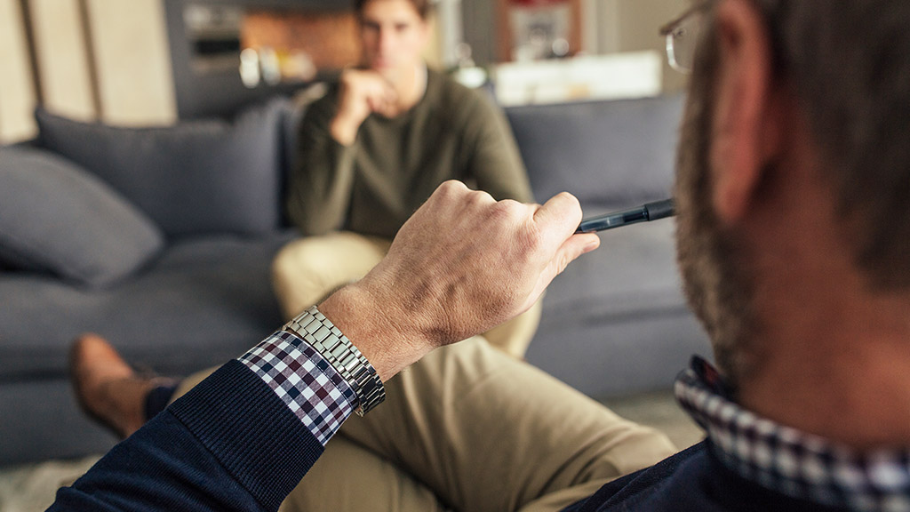 Hands of psychologist holding a pen and listening to man during therapy session