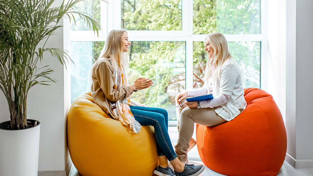 Young woman with senior female psychologist or mental coach sitting on the comfortable chairs during the psychological counseling in the office