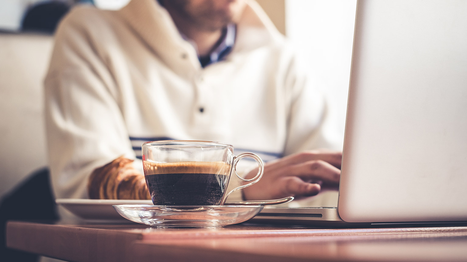 A person drinking a coffee and reading information on a laptop