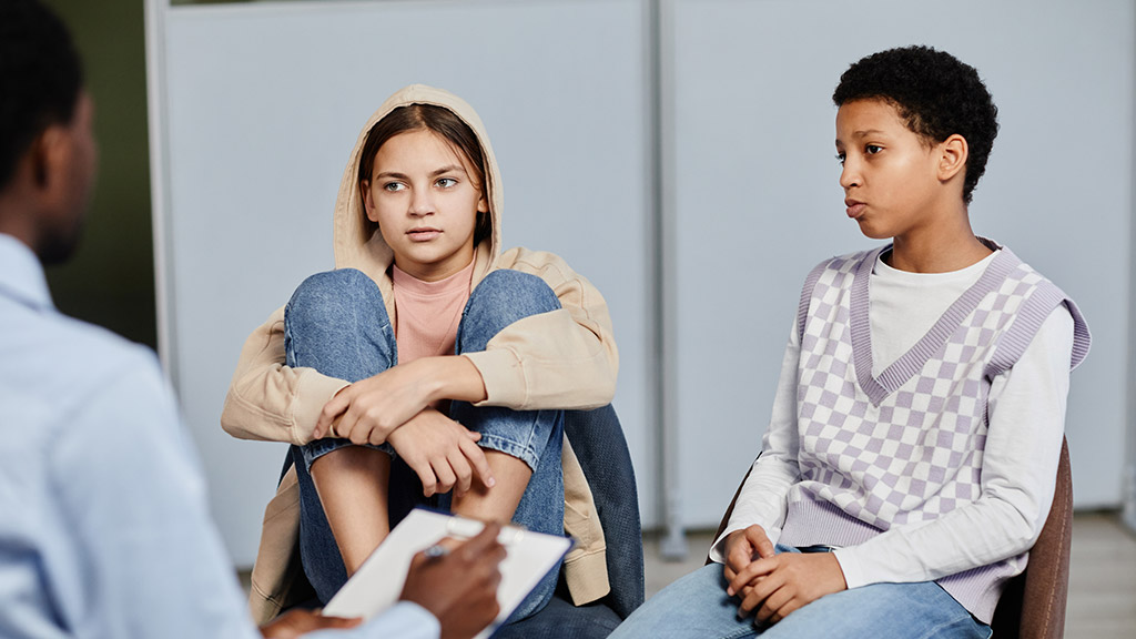 Portrait of two teenage girls speaking to psychologist in therapy session